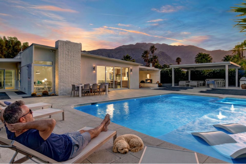 A homeowner relaxing poolside with his dog at a mid-century Palm Springs home